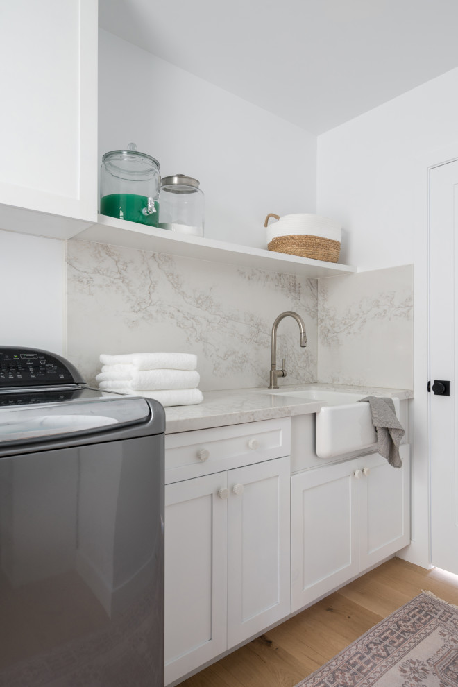 Esempio di un'ampia sala lavanderia stile marinaro con lavello stile country, ante con bugna sagomata, ante bianche, top in quarzo composito, paraspruzzi in quarzo composito, pareti bianche, parquet chiaro e lavatrice e asciugatrice affiancate