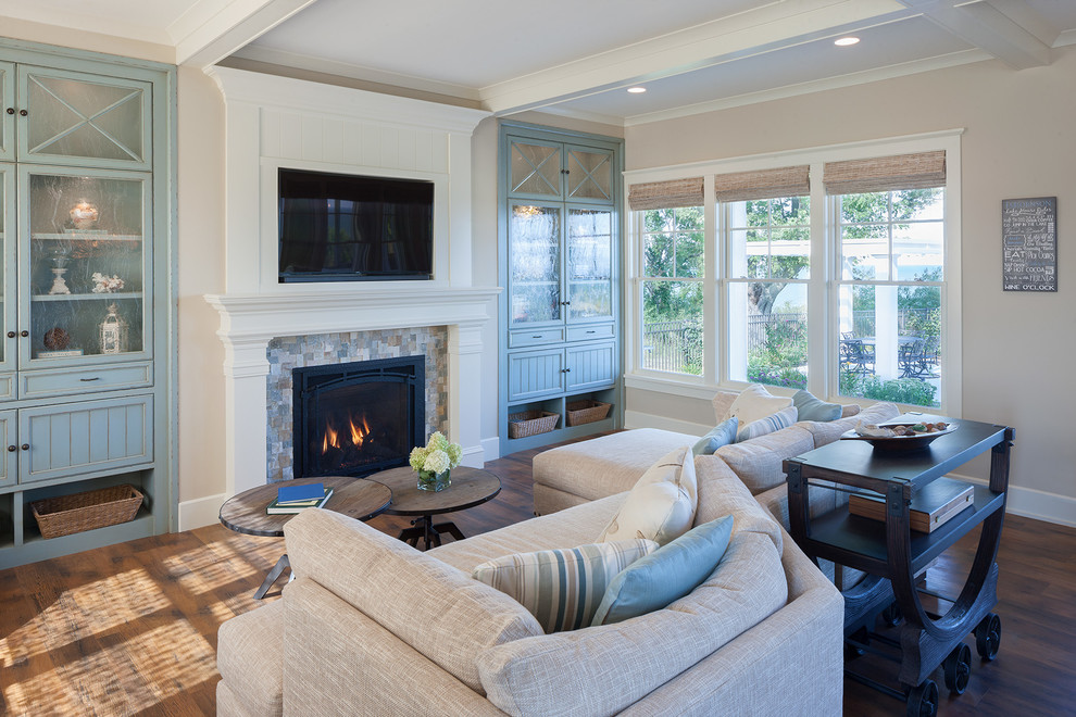 This is an example of a beach style family room in Grand Rapids with beige walls, dark hardwood floors, a standard fireplace, a tile fireplace surround, a built-in media wall and brown floor.