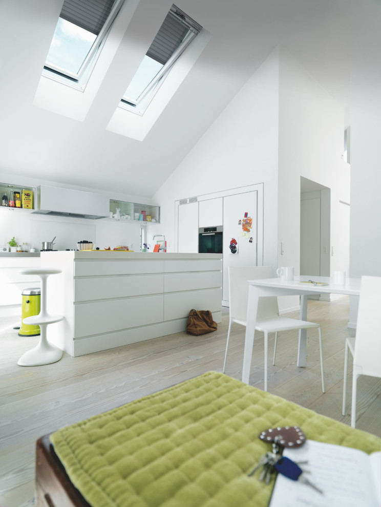 Zweizeilige, Große Moderne Wohnküche mit flächenbündigen Schrankfronten, weißen Schränken, Küchenrückwand in Weiß, schwarzen Elektrogeräten, hellem Holzboden, Kücheninsel und beigem Boden in Düsseldorf