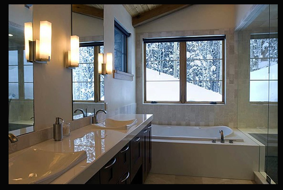 This is an example of a large modern master bathroom in Denver with shaker cabinets, medium wood cabinets, a drop-in tub, an alcove shower, a one-piece toilet, white tile, limestone, white walls, travertine floors, a drop-in sink, solid surface benchtops, white floor and a hinged shower door.