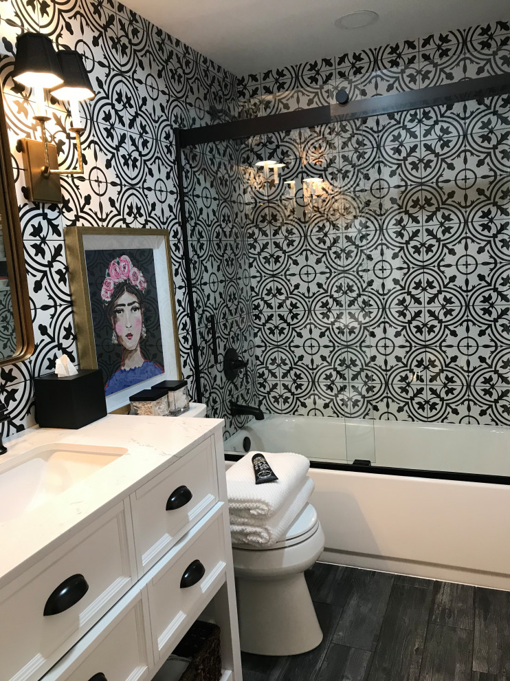 Photo of a mid-sized country master bathroom in Baltimore with shaker cabinets, white cabinets, an alcove tub, a shower/bathtub combo, a two-piece toilet, black and white tile, cement tile, white walls, ceramic floors, an undermount sink, engineered quartz benchtops, black floor, a sliding shower screen, white benchtops, a niche, a single vanity, a freestanding vanity and planked wall panelling.