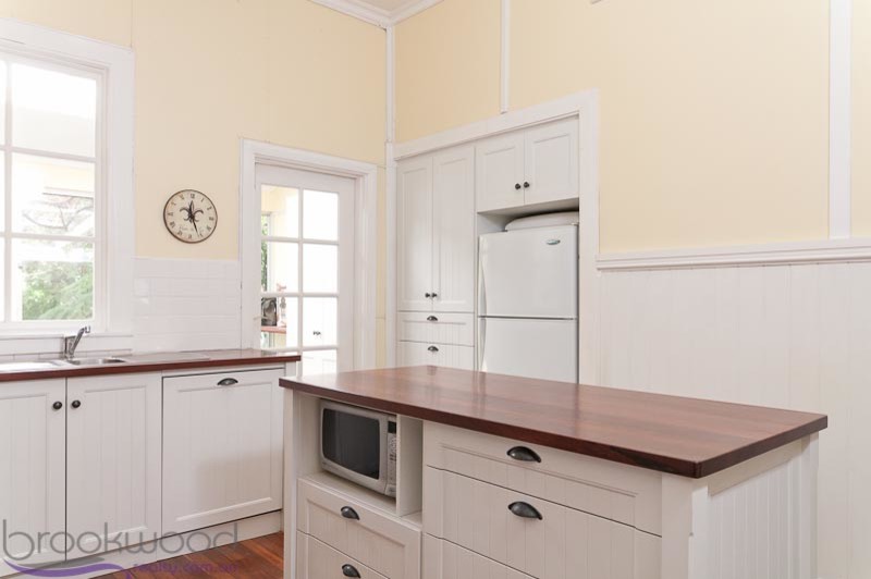 This is an example of a small country u-shaped separate kitchen in Perth with a drop-in sink, white cabinets, wood benchtops, white splashback, ceramic splashback, white appliances, dark hardwood floors and with island.