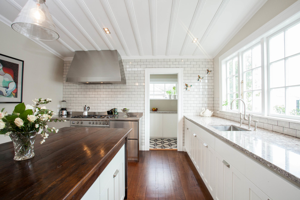 This is an example of a large traditional l-shaped open plan kitchen in Auckland with an undermount sink, white cabinets, white splashback, subway tile splashback, stainless steel appliances, medium hardwood floors, with island and shaker cabinets.