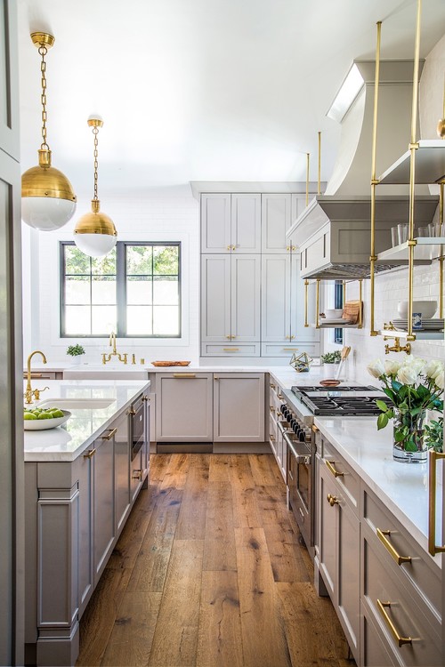 Elegant galley kitchen with light gray shaker RTA cabinets, brass hardware and fixtures, white quartz countertops, subway-tile backsplash, open brass shelving, and wide-plank wood floors.