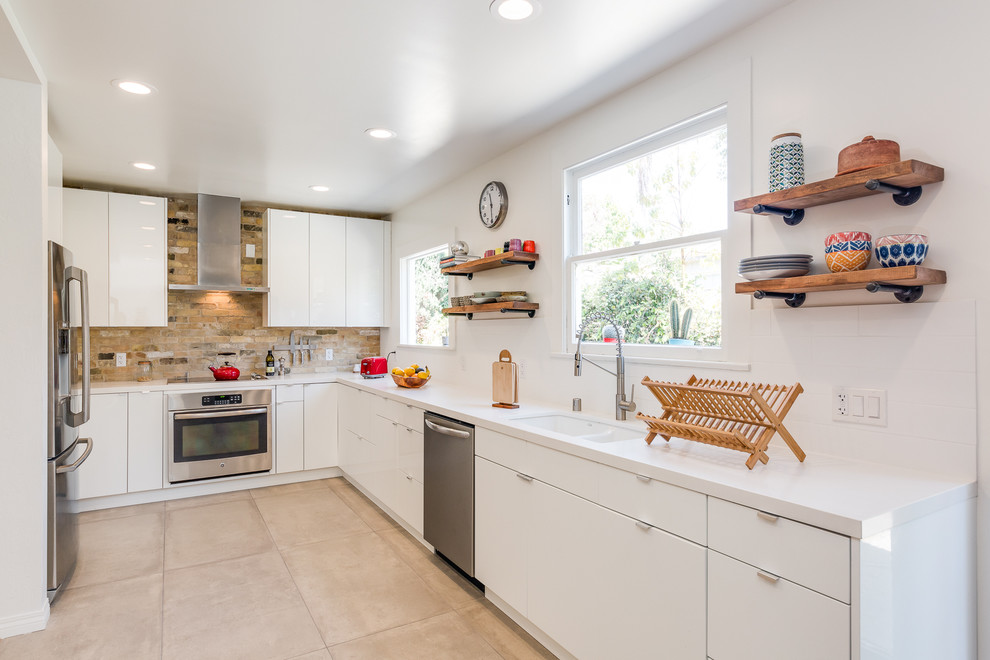 Photo of a mid-sized modern l-shaped eat-in kitchen in San Francisco with a double-bowl sink, flat-panel cabinets, white cabinets, solid surface benchtops, multi-coloured splashback, terra-cotta splashback, stainless steel appliances, terra-cotta floors, no island, beige floor and white benchtop.