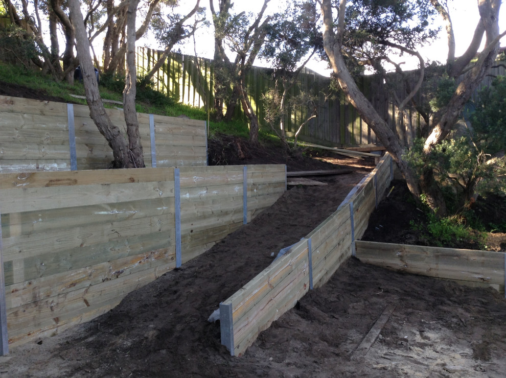 Expansive contemporary back formal fully shaded garden for summer in Melbourne with a retaining wall and a wood fence.