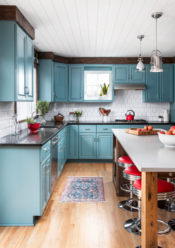 Design ideas for a mid-sized eclectic u-shaped open plan kitchen in Chicago with an undermount sink, raised-panel cabinets, blue cabinets, quartz benchtops, white splashback, ceramic splashback, coloured appliances, light hardwood floors, with island and grey benchtop.