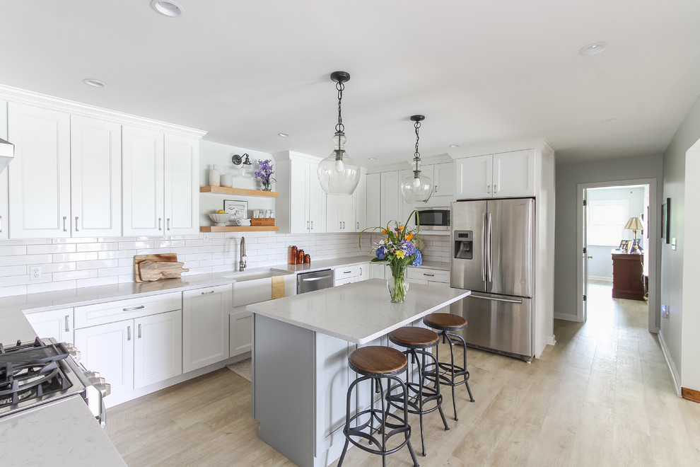 Large country u-shaped separate kitchen in DC Metro with a farmhouse sink, recessed-panel cabinets, white cabinets, quartz benchtops, white splashback, subway tile splashback, stainless steel appliances, vinyl floors, with island and white benchtop.