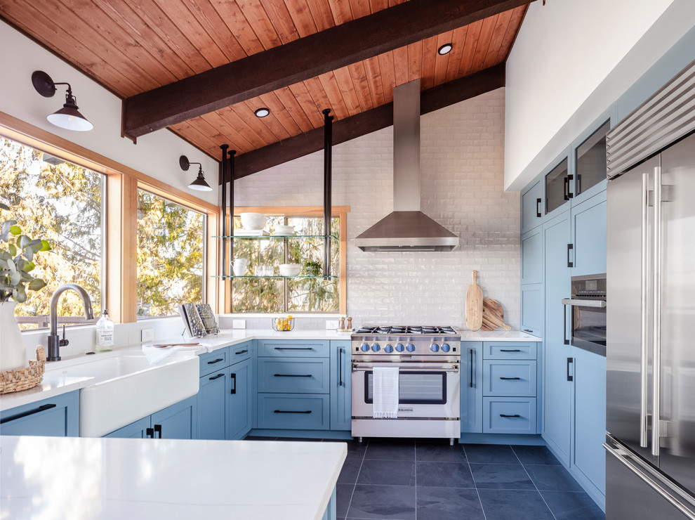 Design ideas for a mid-sized country u-shaped kitchen in Seattle with a farmhouse sink, shaker cabinets, blue cabinets, stainless steel appliances, grey floor, white benchtop, white splashback, a peninsula, quartz benchtops, subway tile splashback and porcelain floors.