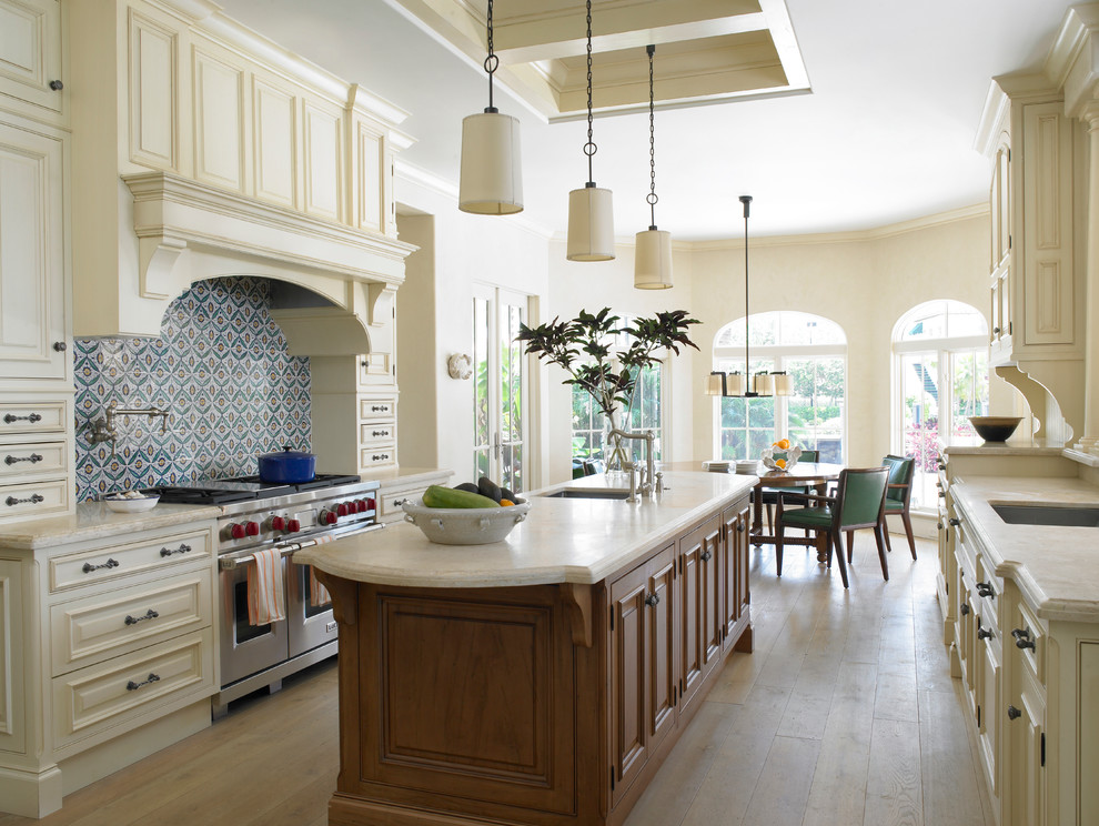Inspiration for a large mediterranean galley eat-in kitchen in Miami with an undermount sink, raised-panel cabinets, beige cabinets, multi-coloured splashback, stainless steel appliances, light hardwood floors, with island, granite benchtops, mosaic tile splashback and beige floor.