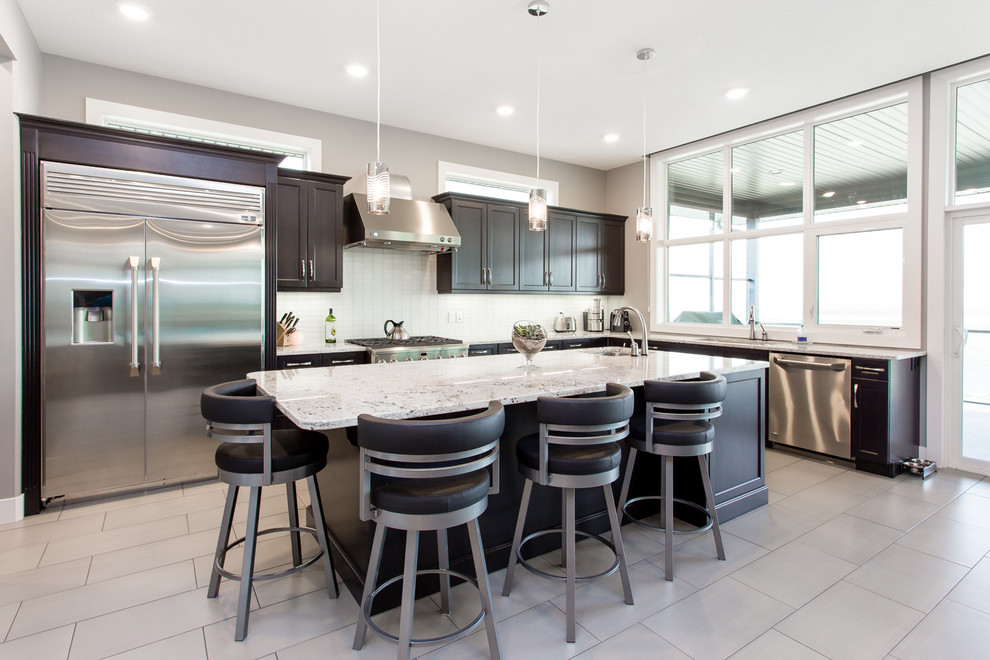 Photo of a large modern l-shaped open plan kitchen in Calgary with an undermount sink, shaker cabinets, dark wood cabinets, granite benchtops, white splashback, glass sheet splashback, stainless steel appliances, porcelain floors and with island.