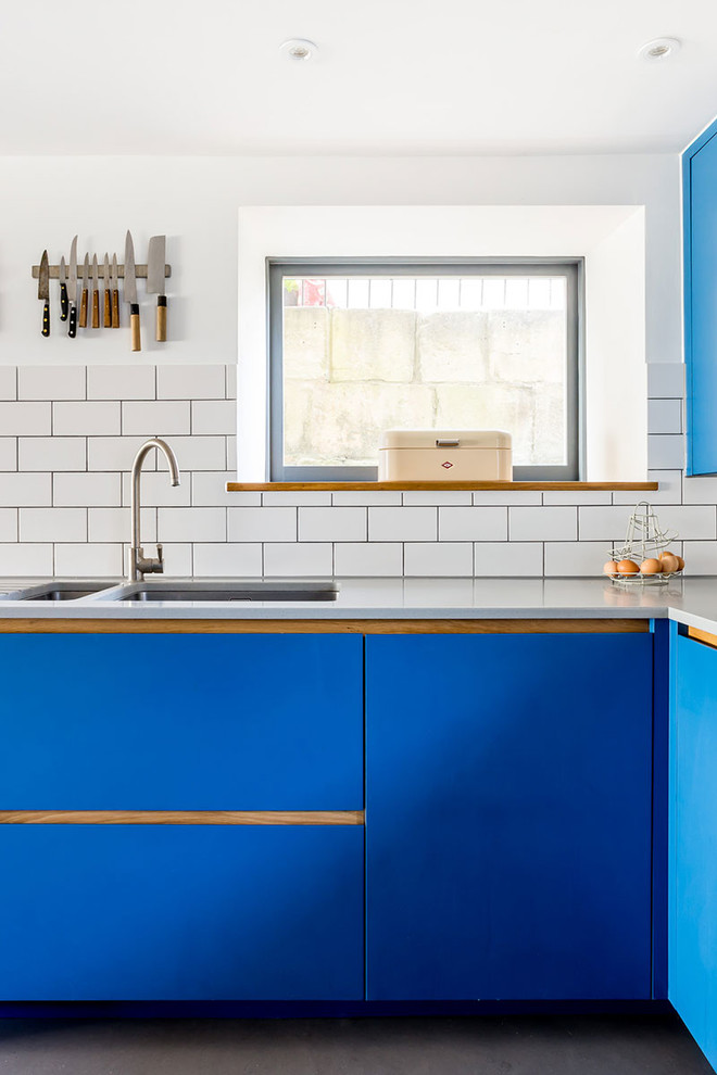 Mid-sized contemporary u-shaped eat-in kitchen in Wiltshire with an undermount sink, flat-panel cabinets, blue cabinets, white splashback, stone tile splashback, stainless steel appliances, concrete floors and no island.