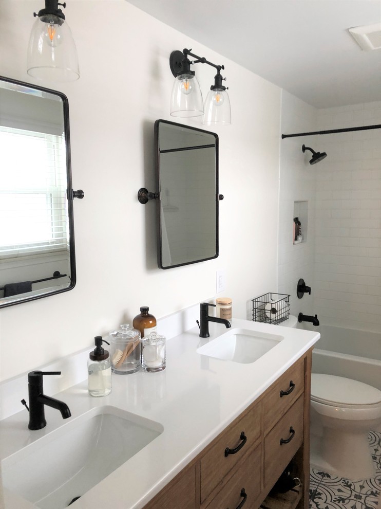 This is an example of a small eclectic master bathroom in Detroit with furniture-like cabinets, medium wood cabinets, an alcove tub, a shower/bathtub combo, a two-piece toilet, white tile, subway tile, white walls, cement tiles, an undermount sink, engineered quartz benchtops, multi-coloured floor, a shower curtain and white benchtops.