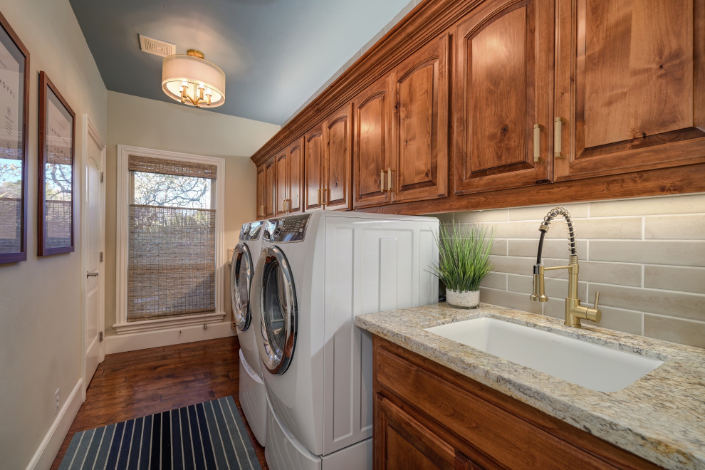 Design ideas for a mid-sized transitional laundry room in Sacramento with a single-bowl sink, raised-panel cabinets, medium wood cabinets, granite benchtops, beige splashback, ceramic splashback, beige walls, dark hardwood floors, a side-by-side washer and dryer, brown floor and beige benchtop.
