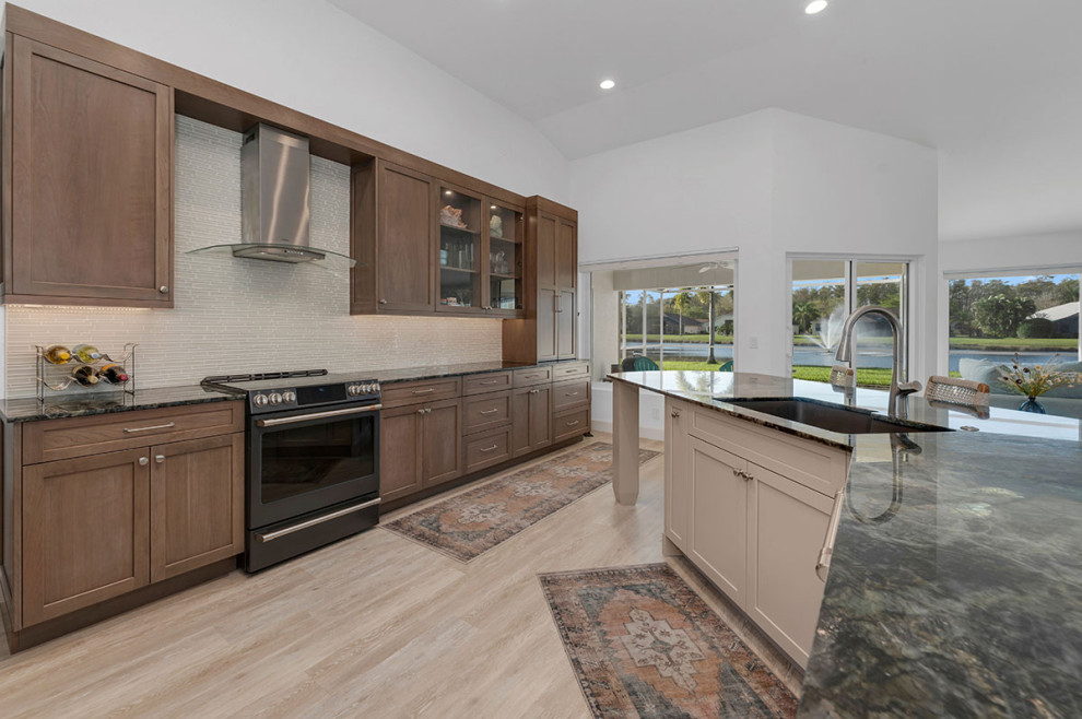 Expansive contemporary single-wall open plan kitchen in Miami with an undermount sink, shaker cabinets, medium wood cabinets, quartzite benchtops, beige splashback, glass sheet splashback, black appliances, vinyl floors, with island, beige floor and multi-coloured benchtop.