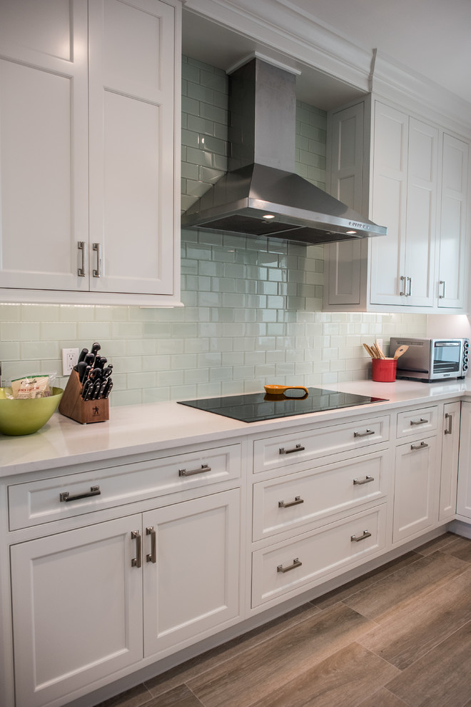 Photo of a mid-sized transitional l-shaped eat-in kitchen in Other with an undermount sink, shaker cabinets, white cabinets, solid surface benchtops, green splashback, glass tile splashback, stainless steel appliances, medium hardwood floors and with island.