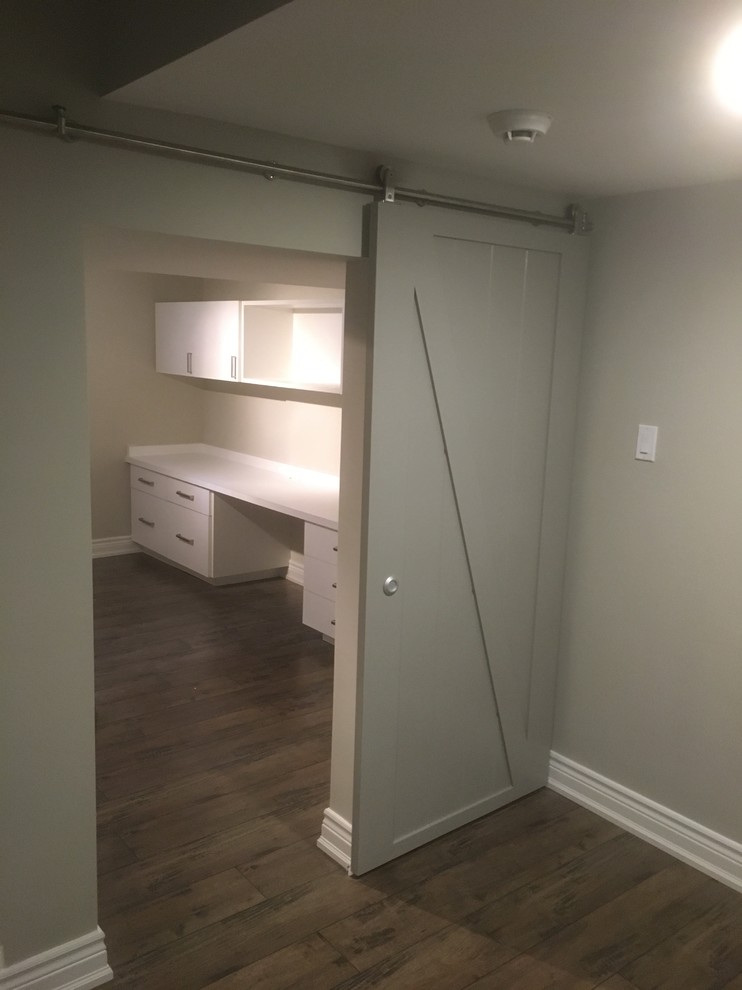 This is an example of a mid-sized transitional craft room in Toronto with beige walls, dark hardwood floors, no fireplace, a built-in desk and brown floor.
