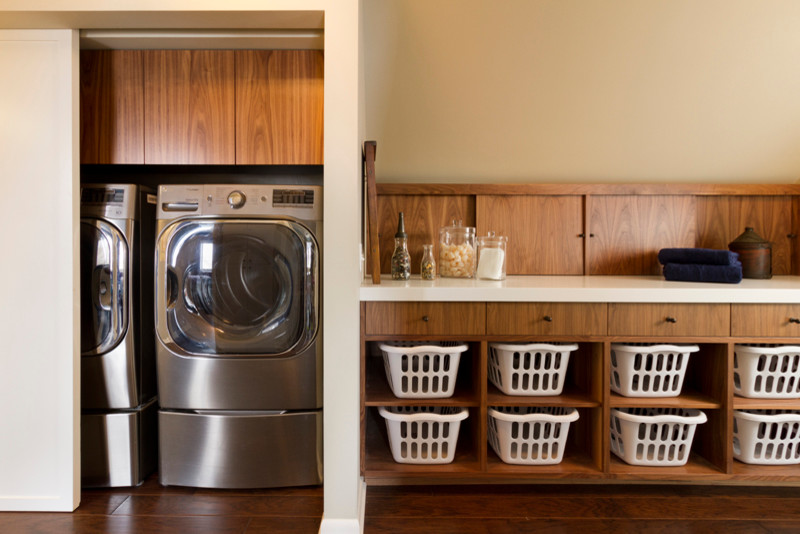 Design ideas for a mid-sized contemporary single-wall dedicated laundry room in Minneapolis with flat-panel cabinets, medium wood cabinets, quartz benchtops, grey walls, dark hardwood floors and a concealed washer and dryer.