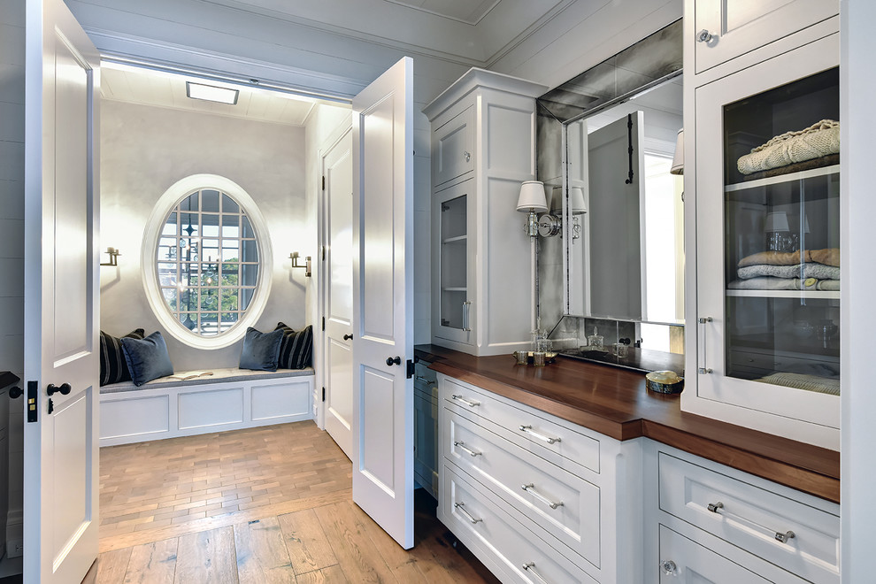 Inspiration for a beach style gender-neutral dressing room in Charleston with glass-front cabinets, white cabinets and medium hardwood floors.