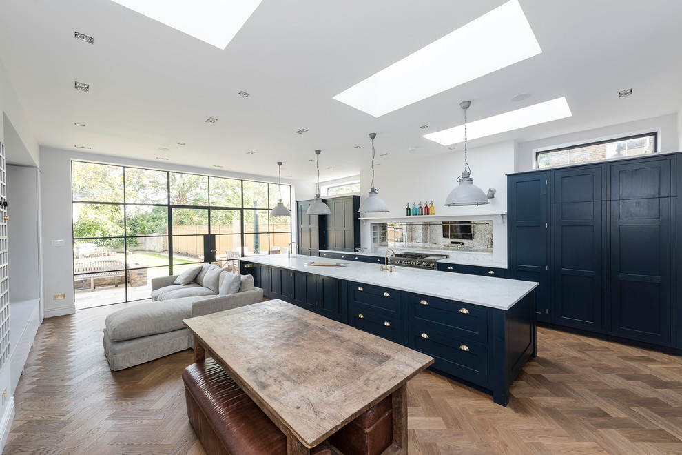 Inspiration for a large transitional open plan kitchen in London with a drop-in sink, shaker cabinets, blue cabinets, marble benchtops, light hardwood floors and with island.