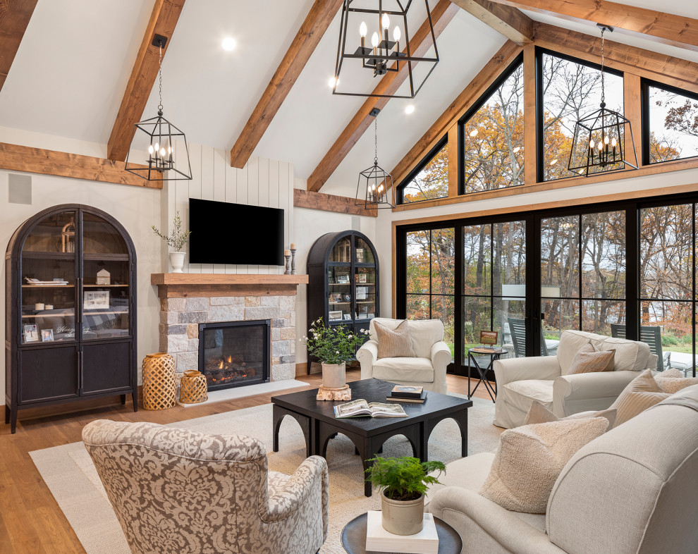 Photo of a large beach style open concept living room in Minneapolis with medium hardwood floors, a standard fireplace, a stone fireplace surround, a wall-mounted tv, brown floor and vaulted.