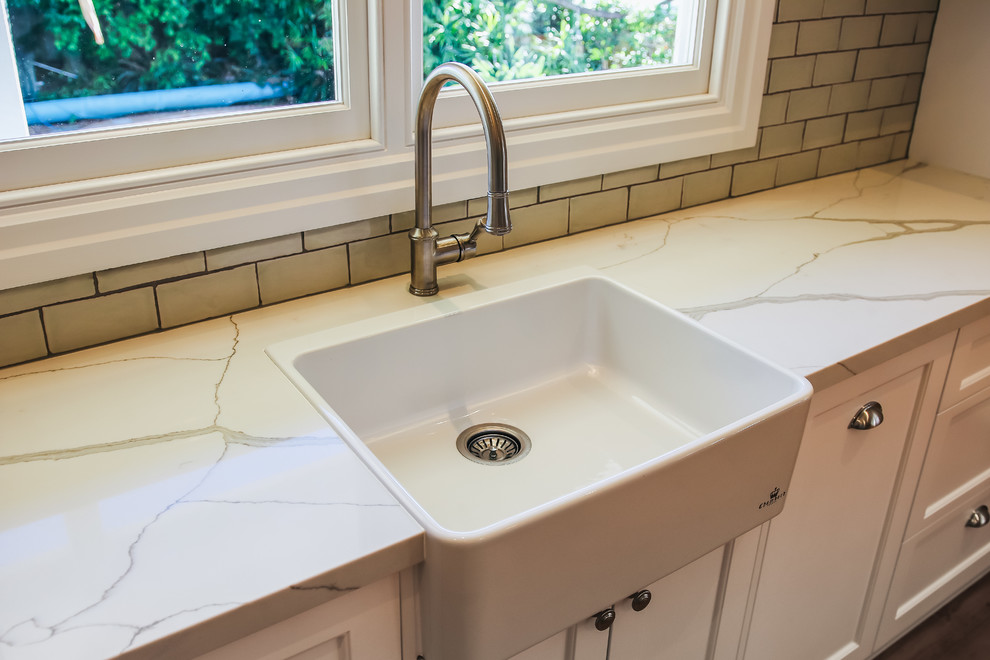 This is an example of a large traditional l-shaped eat-in kitchen in Brisbane with a farmhouse sink, shaker cabinets, green cabinets, quartz benchtops, green splashback, subway tile splashback, white appliances, medium hardwood floors, with island and green benchtop.