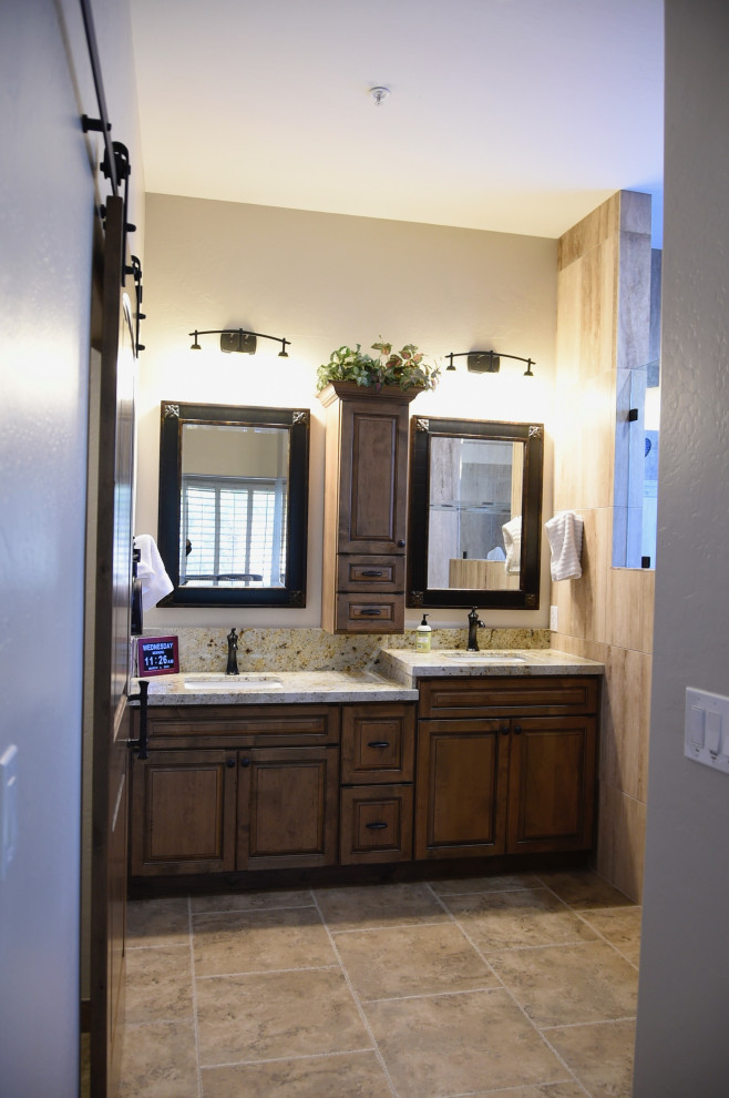Mid-sized transitional master bathroom in Phoenix with raised-panel cabinets, medium wood cabinets, beige tile, stone tile, grey walls, porcelain floors, an undermount sink, granite benchtops, brown floor, multi-coloured benchtops, a shower seat, a double vanity and a built-in vanity.