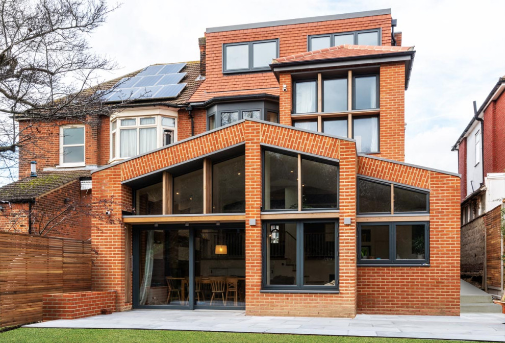 Expansive contemporary three-storey brick red duplex exterior in London with a gable roof, a tile roof and a red roof.