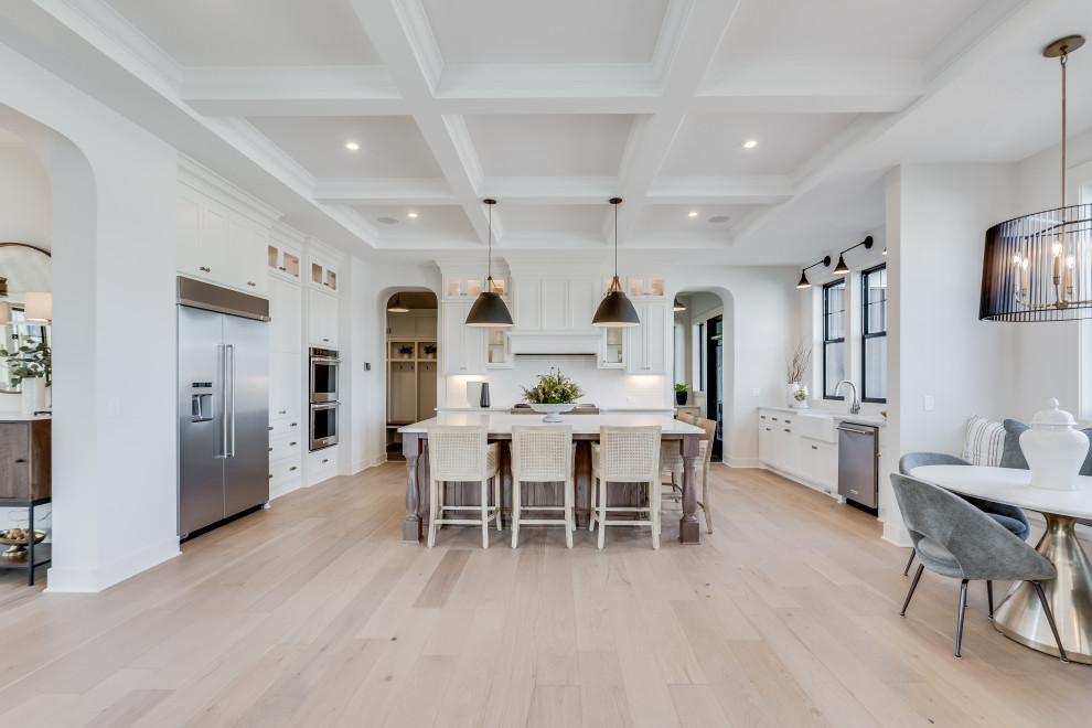 Design ideas for a large country eat-in kitchen in Minneapolis with a farmhouse sink, white cabinets, white splashback, granite splashback, stainless steel appliances, light hardwood floors, with island, brown floor, white benchtop and vaulted.