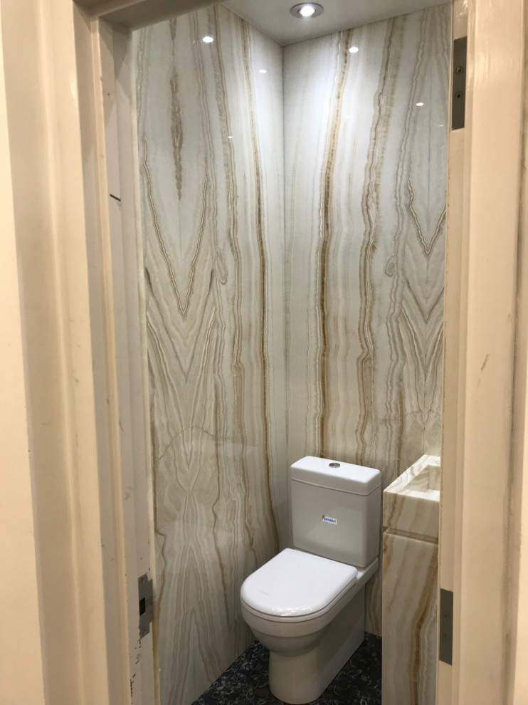 Small modern cloakroom in New York with flat-panel cabinets, beige cabinets, a one-piece toilet, beige tiles, marble tiles, beige walls, slate flooring, an integrated sink, marble worktops, black floors, beige worktops, a freestanding vanity unit, a drop ceiling and panelled walls.