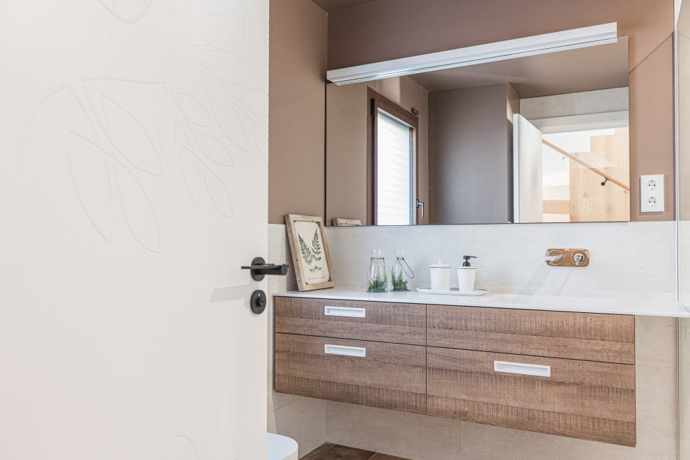 This is an example of a mid-sized contemporary 3/4 bathroom in Barcelona with flat-panel cabinets, white cabinets, a drop-in tub, a curbless shower, a wall-mount toilet, beige tile, ceramic tile, brown walls, ceramic floors, an undermount sink, engineered quartz benchtops, brown floor, a sliding shower screen, white benchtops, an enclosed toilet, a double vanity and a floating vanity.