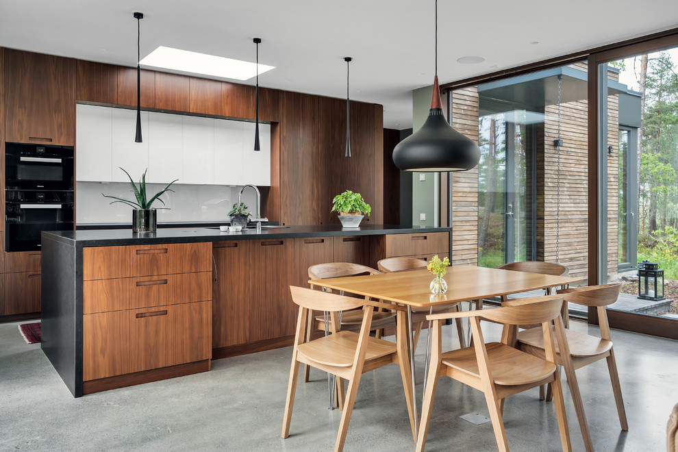 Mid-sized contemporary galley eat-in kitchen in Stockholm with flat-panel cabinets, medium wood cabinets, concrete floors, with island, grey floor, black benchtop, an undermount sink, white splashback and black appliances.