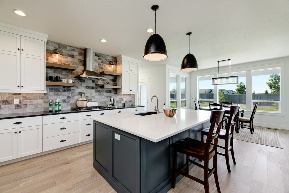 Transitional eat-in kitchen in Boise with an undermount sink, shaker cabinets, white cabinets, multi-coloured splashback, light hardwood floors, with island, beige floor and black benchtop.
