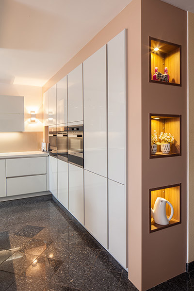 Küche in L-Form mit integriertem Waschbecken, flächenbündigen Schrankfronten, weißen Schränken, Quarzwerkstein-Arbeitsplatte, Küchenrückwand in Beige, Küchengeräten aus Edelstahl, Marmorboden, Kücheninsel, Glasrückwand und schwarzem Boden