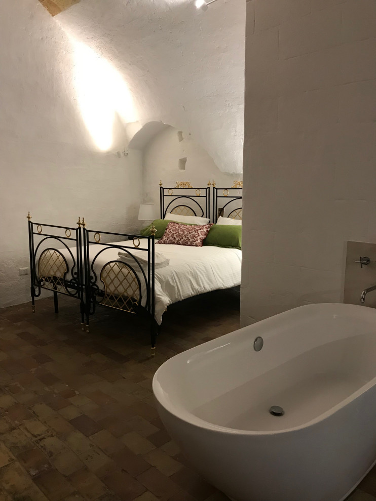 Foto di un'ampia camera matrimoniale mediterranea con pareti bianche, camino classico, soffitto a volta e pareti in mattoni