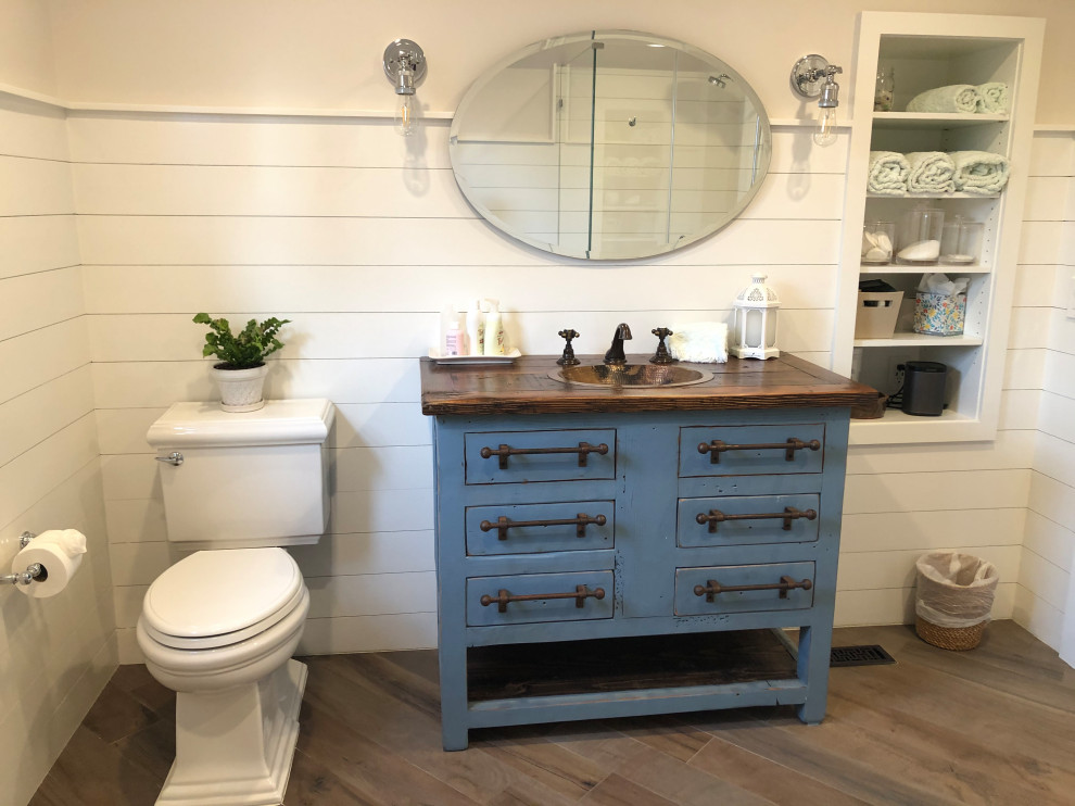 Photo of a large transitional master bathroom in Newark with furniture-like cabinets, turquoise cabinets, a corner tub, a corner shower, a one-piece toilet, white tile, white walls, light hardwood floors, a drop-in sink, wood benchtops, brown floor, a hinged shower door, brown benchtops, a niche, a single vanity, a freestanding vanity and planked wall panelling.