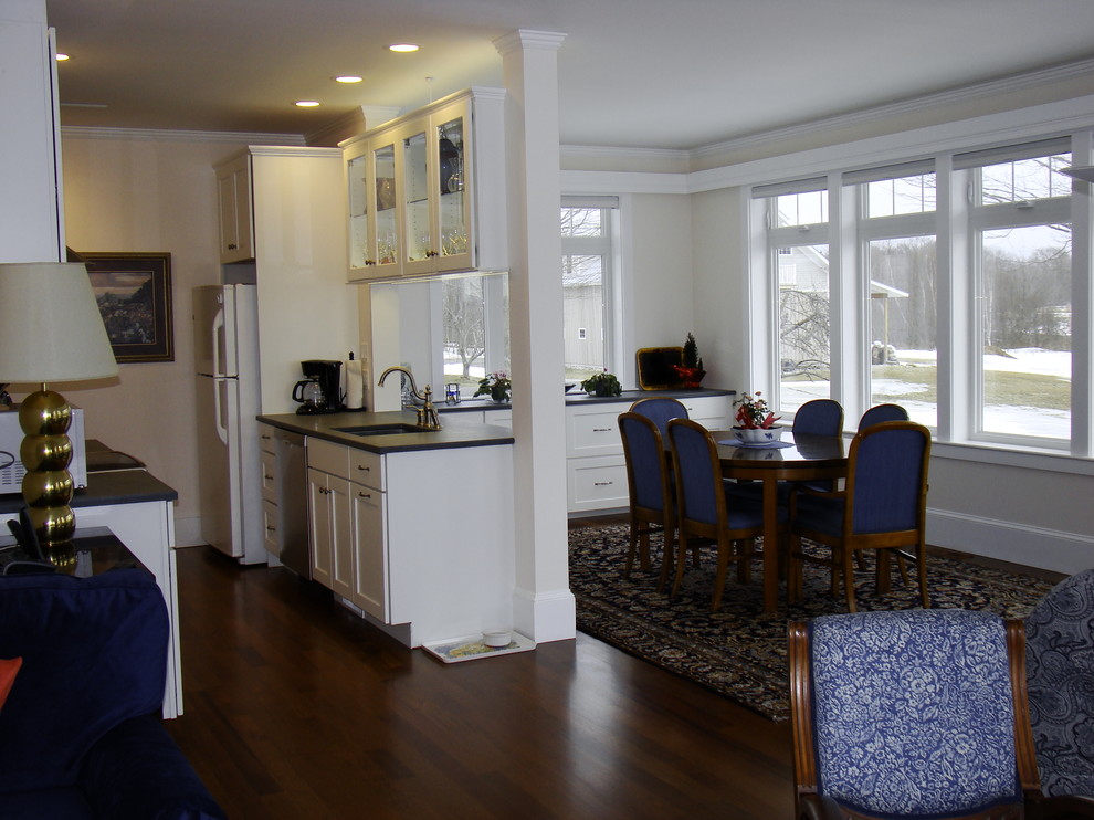 Photo of a small traditional galley open plan kitchen in Portland Maine with an undermount sink, shaker cabinets, white cabinets, granite benchtops, white appliances, dark hardwood floors and no island.