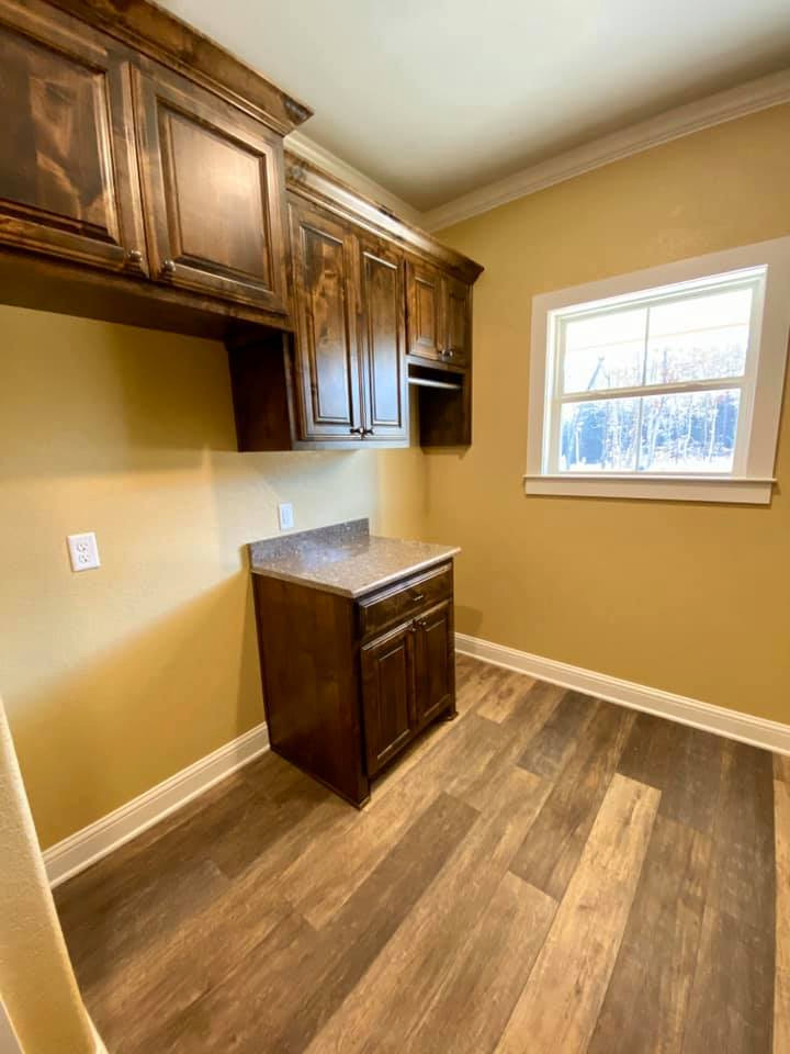 Photo of a country galley dedicated laundry room in Dallas with raised-panel cabinets, medium wood cabinets, granite benchtops, yellow walls, vinyl floors, brown floor and brown benchtop.