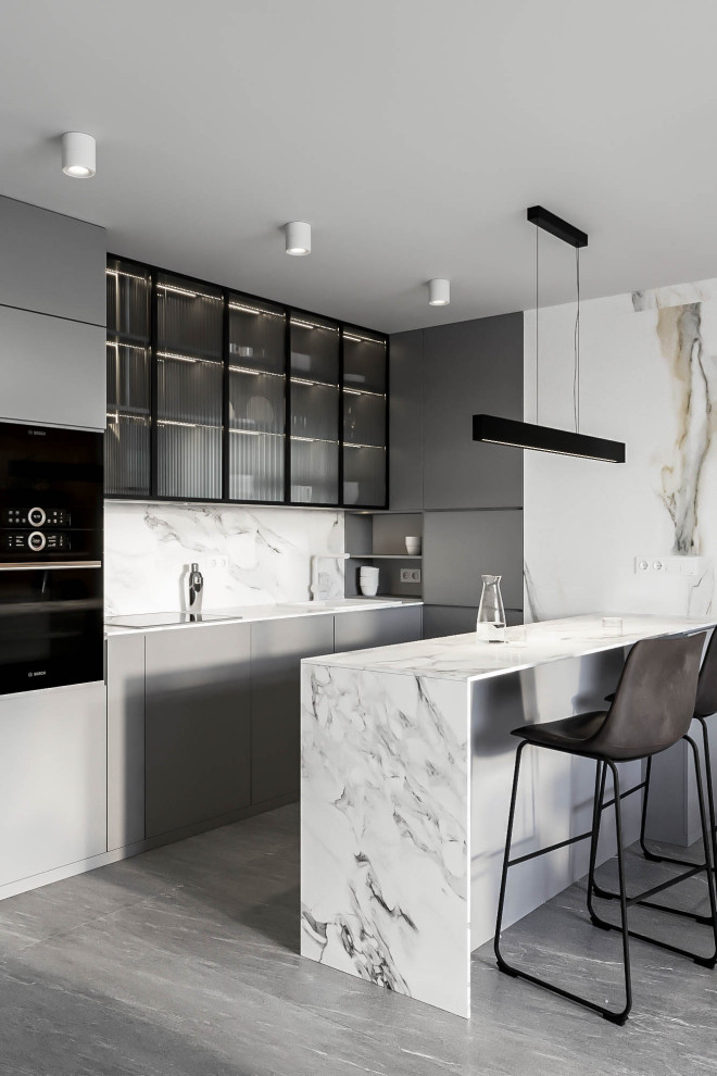 This is an example of a mid-sized modern galley open plan kitchen in Valencia with an integrated sink, glass-front cabinets, grey cabinets, tile benchtops, multi-coloured splashback, porcelain splashback, black appliances, porcelain floors, with island, grey floor and multi-coloured benchtop.