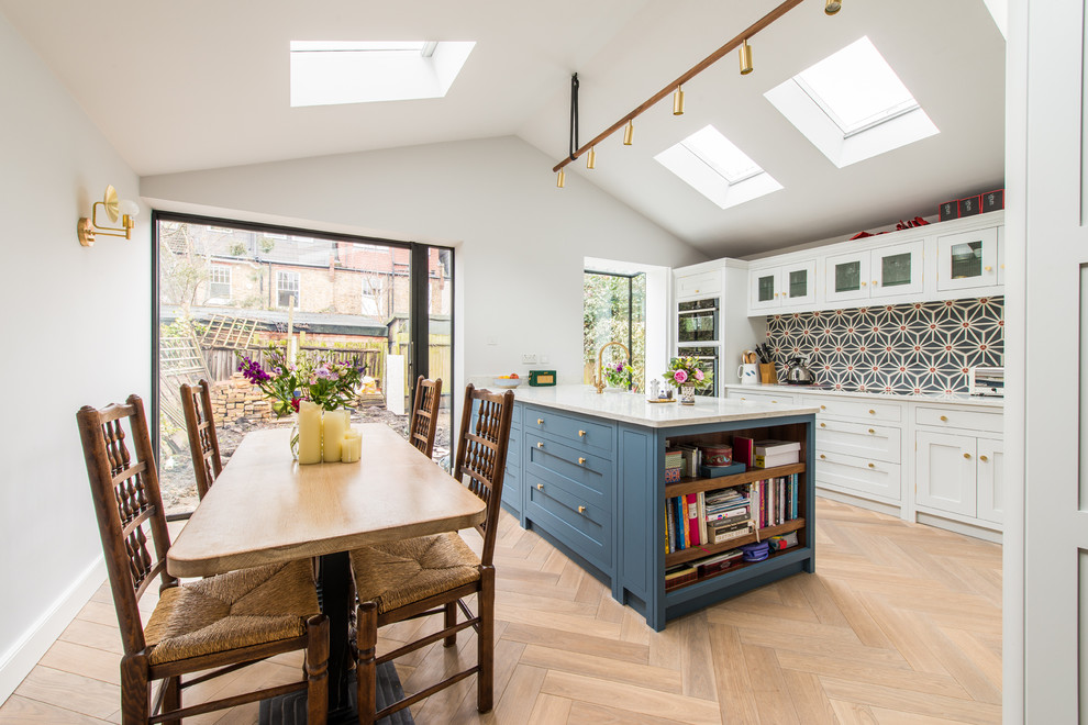 Photo of a transitional galley eat-in kitchen in Kent with shaker cabinets, blue cabinets, blue splashback, ceramic splashback, black appliances, light hardwood floors, with island and white benchtop.