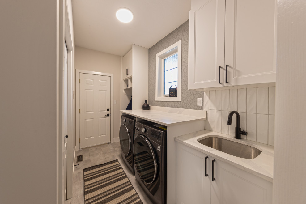 This is an example of a mid-sized country single-wall utility room in Edmonton with an undermount sink, recessed-panel cabinets, white cabinets, quartz benchtops, white splashback, ceramic splashback, multi-coloured walls, ceramic floors, a side-by-side washer and dryer, grey floor and white benchtop.