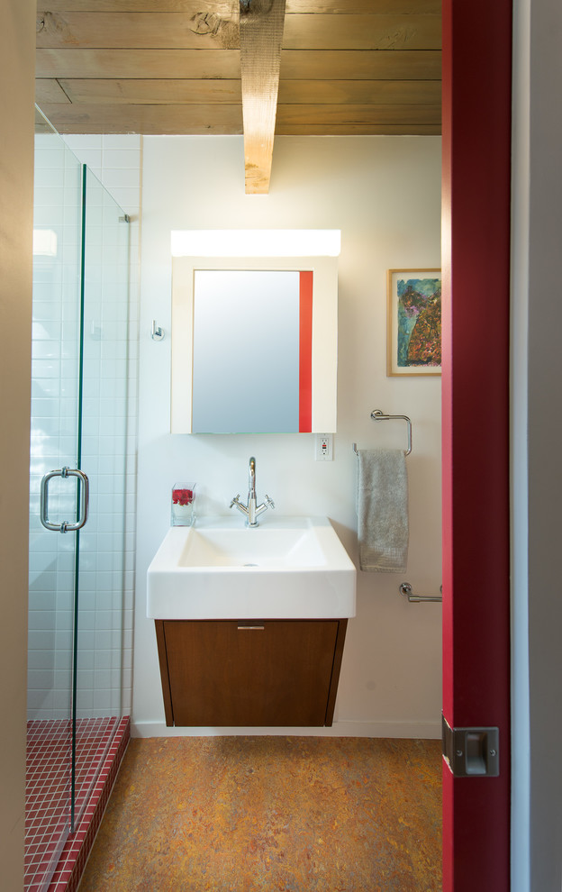 Photo of a midcentury bathroom in Denver with recessed-panel cabinets, medium wood cabinets, a wall-mount toilet, white tile, subway tile, white walls, linoleum floors, a vessel sink and a hinged shower door.