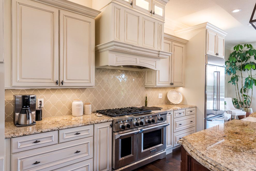 This is an example of a large transitional single-wall eat-in kitchen in Dallas with a farmhouse sink, raised-panel cabinets, white cabinets, granite benchtops, beige splashback, ceramic splashback, stainless steel appliances, dark hardwood floors, with island and brown floor.