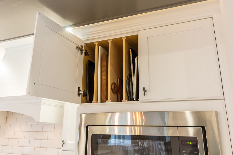 Example of a large transitional u-shaped medium tone wood floor and brown floor enclosed kitchen design with an undermount sink, shaker cabinets, white cabinets, quartzite countertops, white backsplash, subway tile backsplash, stainless steel appliances and an island