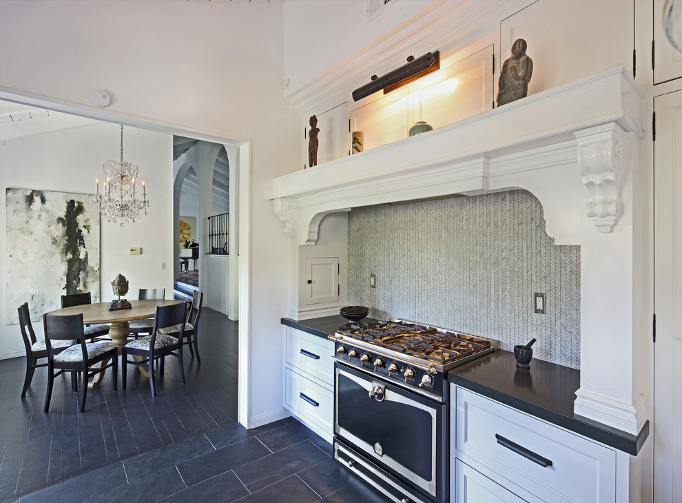 This is an example of a traditional eat-in kitchen in Los Angeles with recessed-panel cabinets, white cabinets, grey splashback and black appliances.