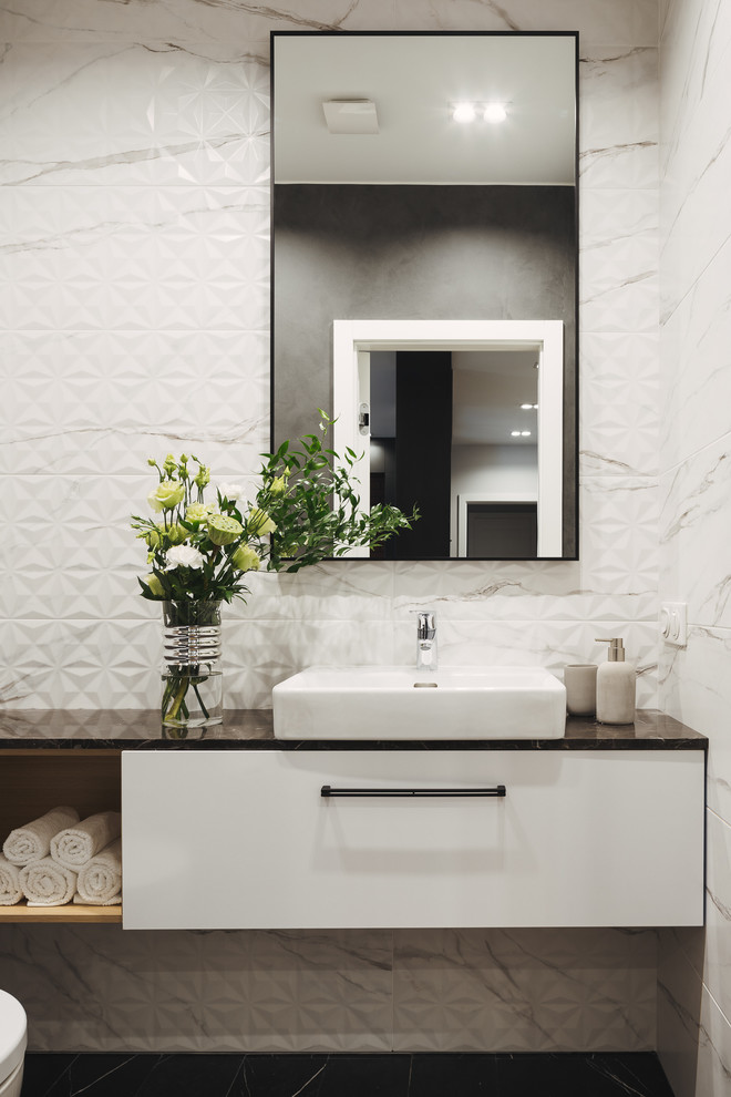 This is an example of a contemporary powder room in Saint Petersburg with flat-panel cabinets, white cabinets, white tile, white walls, a vessel sink, black floor and black benchtops.