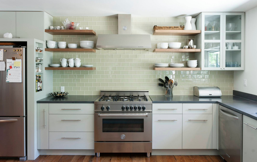 Transitional medium tone wood floor kitchen photo with flat-panel cabinets, white cabinets, solid surface countertops, green backsplash, glass tile backsplash and stainless steel appliances
