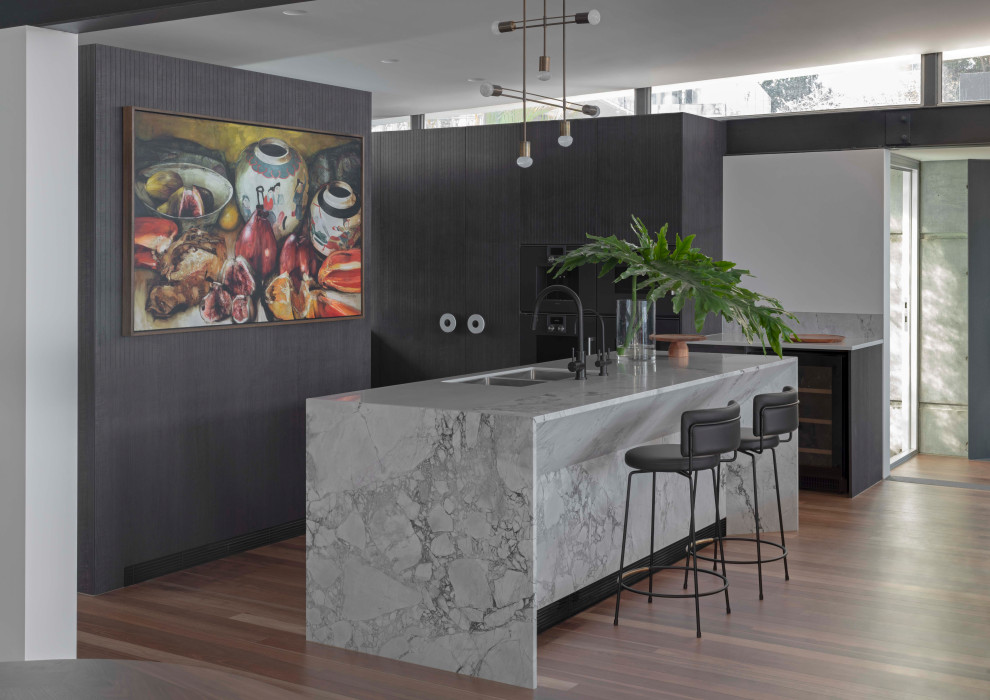 Photo of a large contemporary u-shaped kitchen in Sydney with a double-bowl sink, flat-panel cabinets, dark wood cabinets, marble benchtops, glass sheet splashback, panelled appliances, medium hardwood floors, with island, brown floor, grey benchtop and exposed beam.