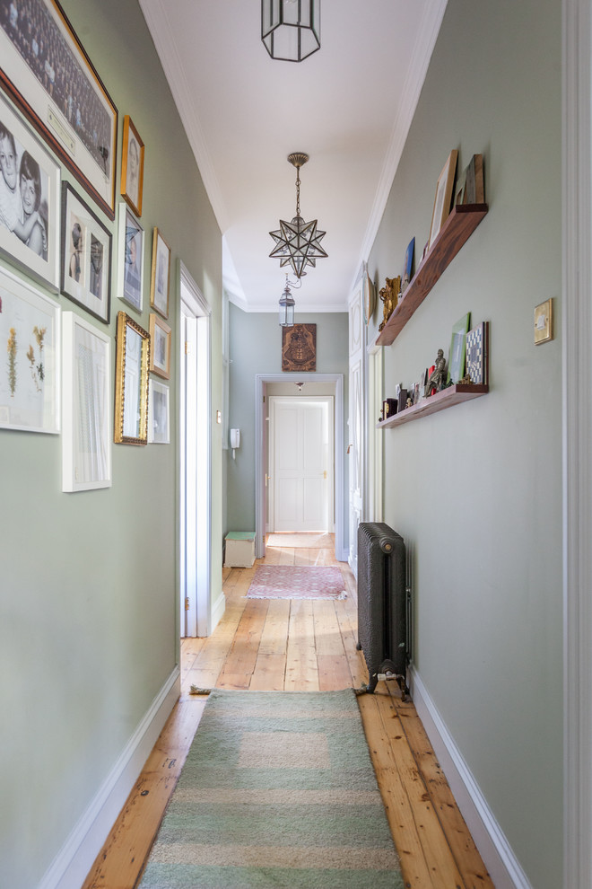 Photo of a transitional hallway in London with green walls and medium hardwood floors.