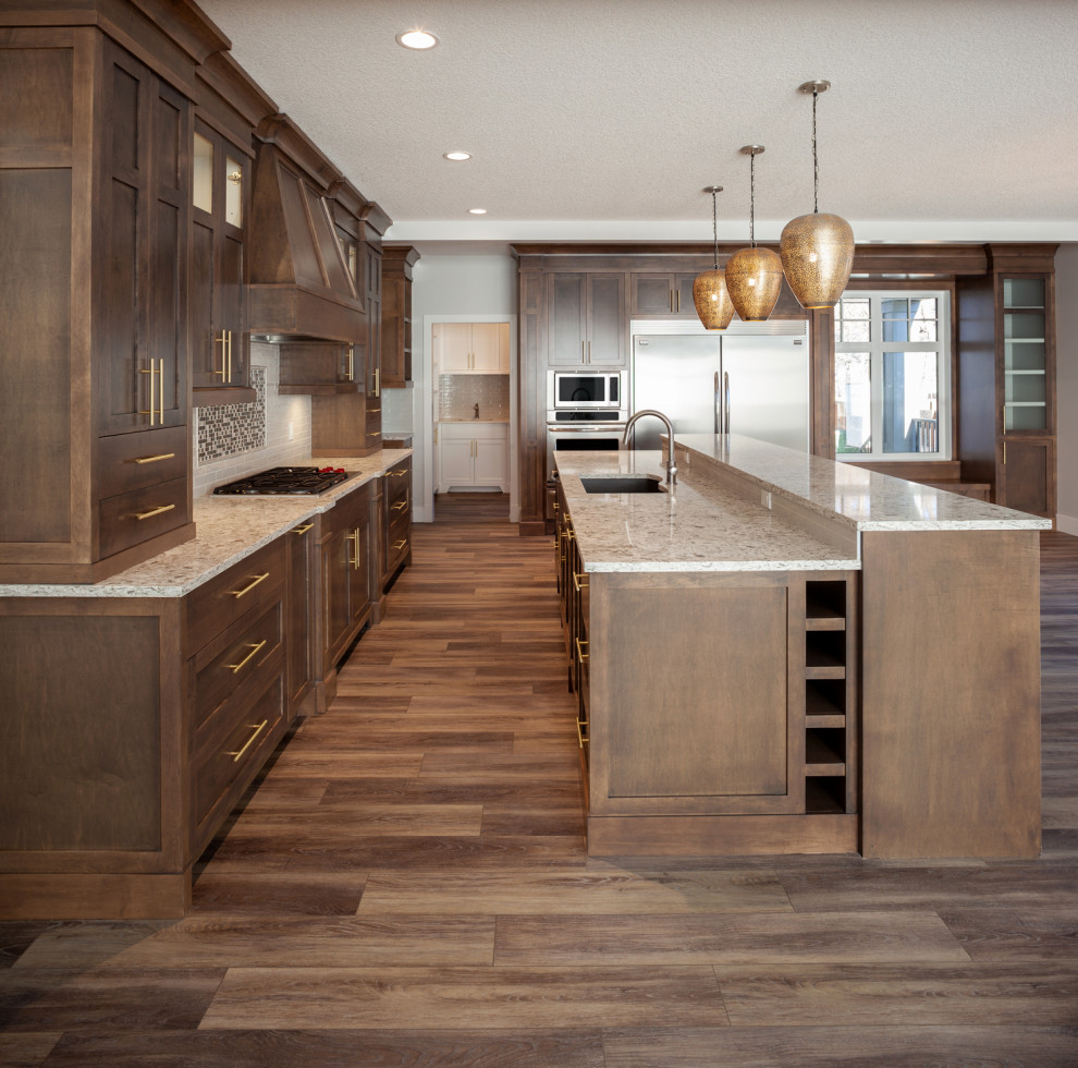 This is an example of a mid-sized arts and crafts l-shaped eat-in kitchen in Calgary with an undermount sink, recessed-panel cabinets, dark wood cabinets, marble benchtops, multi-coloured splashback, ceramic splashback, stainless steel appliances, dark hardwood floors, with island, brown floor, brown benchtop and recessed.